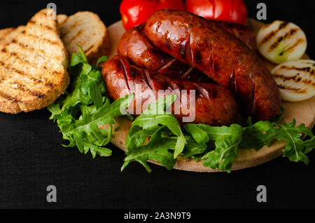 Gegrillte Würstchen mit Rucola und Gemüse auf schwarzem Hintergrund. Kopieren Sie Platz. Stockfoto