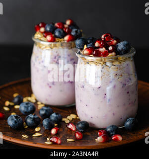 Nahaufnahme von Joghurt mit Blaubeeren, Granatapfel Samen und Hafer auf dunklem Hintergrund. Vorderansicht, quadratischen Bild Stockfoto