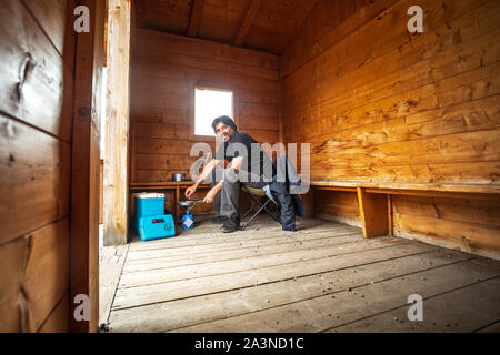 Mann, der Essen auf Campinggas in einer Holzkabine kocht Stockfoto