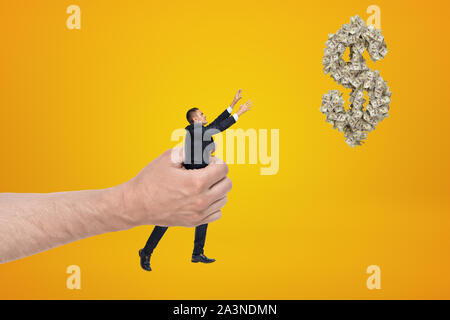 Big Hand kleine Unternehmer erreichen, mit seinen beiden Händen für Dollar Symbol aus Dollarscheine und schwebend in der Luft auf gelben Hintergrund. Stockfoto