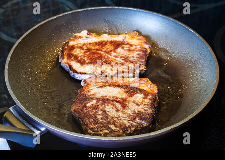 Zwei gebratenes Stück Fleisch in der Pfanne auf Keramik elektrische Reichweite zu Hause Küche Stockfoto