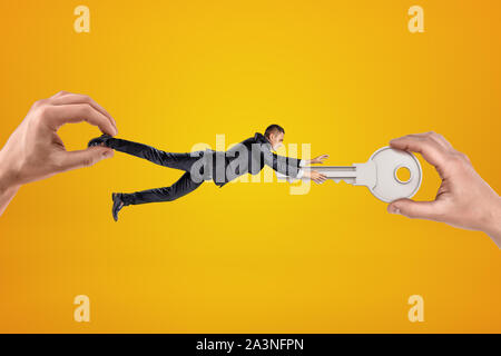 Große männliche Hand kleine Geschäftsmann, der zu einem anderen grossen Hand silber Metall Schlüssel auf gelbem Hintergrund Stockfoto