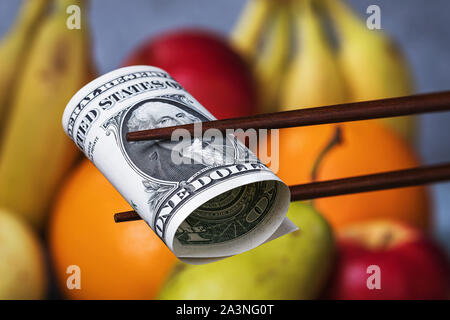 Chinese sticks halten einen Dollar auf einem Hintergrund von Obst. Konzept zum Thema der wirtschaftlichen Konfrontation zwischen Amerika und China. Essen Embargo Stockfoto