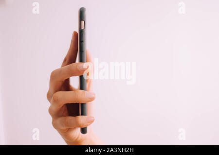 Eine Nahaufnahme der Hand eines jungen Menschen mit einem Handy auf weißem Hintergrund Stockfoto