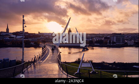 Derry/Londonderry, Nordirland, Großbritannien - 9. Oktober 2019. UK Wetter: Sonne über der Peace Bridge als Fußgänger der Foyle Fluss überqueren. Die Sonne machte eine späte Auftreten nach einer unruhigen Nachmittag. Stockfoto