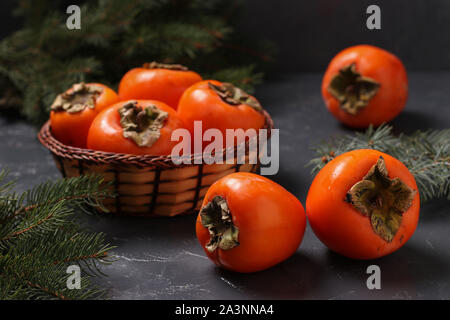 Orange Kaki Früchte auf einer Tabelle und in einem Weidenkorb auf einem dunklen Hintergrund Reif, horizontale Ausrichtung, Nahaufnahme Stockfoto