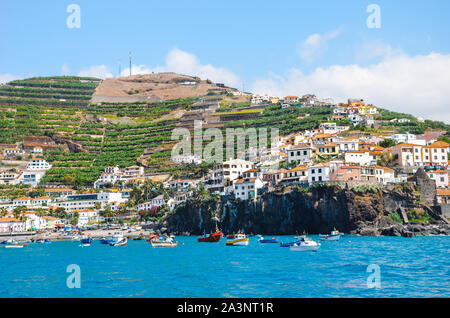 Erstaunlich Dorf Camara de Lobos auf Madeira, Portugal fotografiert von den Gewässern des Atlantik. Kleine Stadt auf einem Hügel an der Küste. Touristische Destination. Bananenplantage auf der Piste. Stockfoto