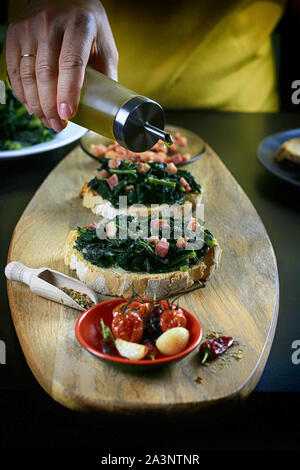 Konzept der italienisches Essen. In der Nähe von Frau Hände gießen Olivenöl über Bruschetta mit schwarzen Kraut und Speck. Rustikale italienische Beilage Stockfoto