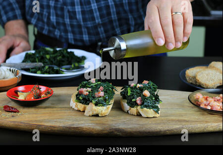 Konzept der italienisches Essen. Nahaufnahme der männlichen Händen gießen Olivenöl über Bruschetta mit schwarzen Kraut und Speck. Rustikale italienische Beilage Stockfoto