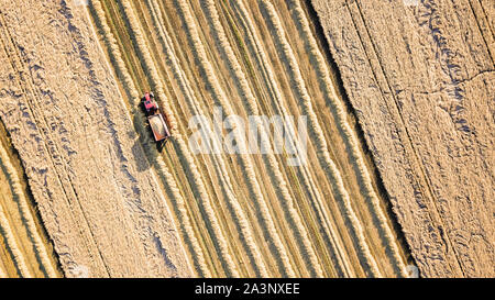 Antenne drone Ansicht von Traktor und Anhänger Pressen von Ballen in einer Northumberland Weizenfeld Stockfoto