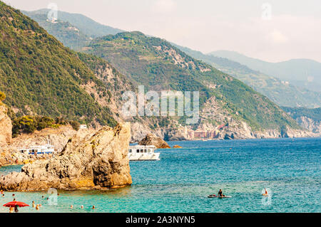 Monterosso al Mare, Italien - September 02, 2019: Die Menschen im Meer schwimmen, Yachten und Boote in der Nähe der felsigen Küste reisen mit grünen Bergen o Stockfoto