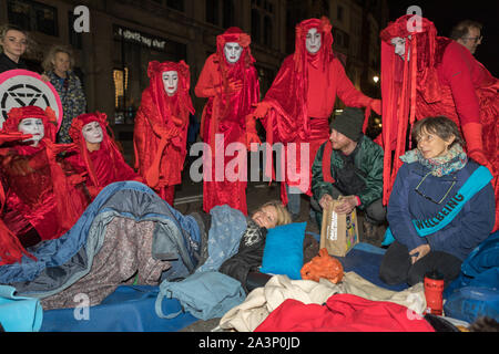 Trafalgar Square, London, Großbritannien. Oktober 2019. Rote Rebellen von Extinction Rebellion führen während der Oktoberaufstand in Whitehall, London, einen feierlichen nächtlichen Protest durch. In fließenden roten Kostümen und weißer Gesichtsfarbe gekleidet, geben sie Gesten zu Aktivisten, die auf dem Bürgersteig ruhen, einige in Decken gehüllt. Ein Wohlbefinden-Koordinator mit einer Schärpe bietet Unterstützung und hebt hervor, dass XR bei ausgedehnten zivilen Ungehorsamsaktionen im Herzen des britischen Regierungsbezirks den Schwerpunkt auf Pflege und Gemeinschaft legt. Penelope Barritt/Alamy Live News Stockfoto