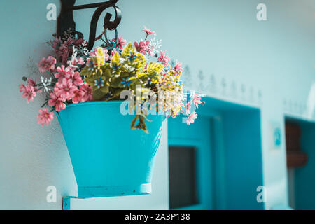 Rosa Blumen in einem blauen Schaufel auf eine weiße Wand, typisch mediterranes Dorf aufgehängt Stockfoto