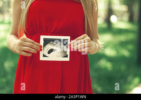 Glückliche junge Erwachsene schwangere Mädchen hält in der Hand einen Snapshot einer Ultraschall eines Kindes. Ersten trimester Stockfoto