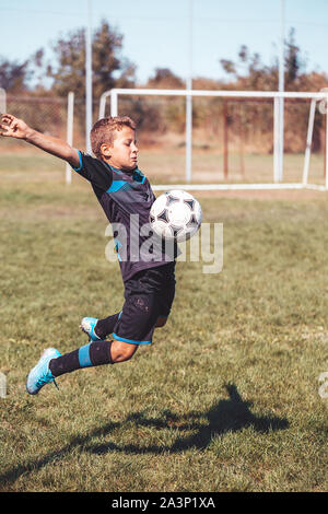 Unter den Ball auf der Brust im Fußball. Jumping little boy in Aktion, Bewegung im Spiel. Junior Football Player springt zum Schlagen der Fußball-Witz Stockfoto