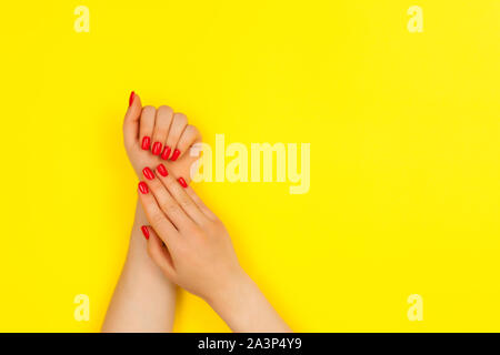 Maniküre an zwei Händen einer Frau auf einem gelben Hintergrund mit Platz für Text. Flach. Stockfoto