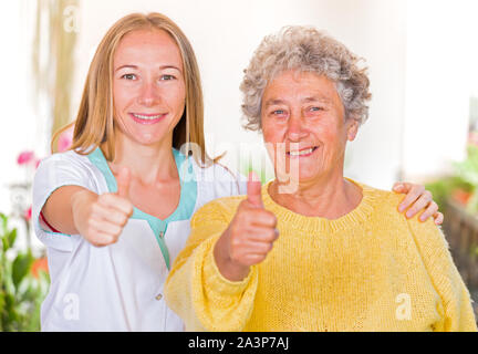 Gerne ältere Frau mit ihrem Pfleger zeigen Daumen hoch Stockfoto
