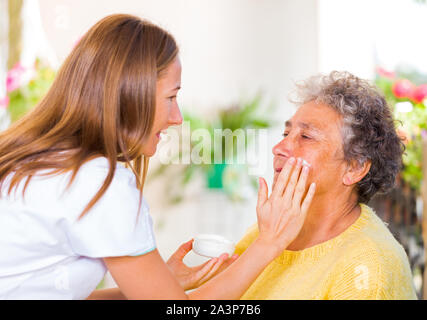 Betreuer reibt sich das Gesicht Creme auf die älteren womans Gesicht Stockfoto