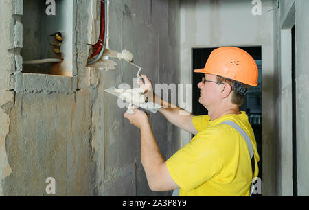 Der Arbeiter ist Holding Kellen mit Gips. Es ist für die elektrische Wellrohre in der Wand. Stockfoto