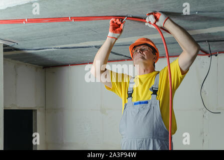 Der Elektriker ist zur Festsetzung einer elektrischen Wellrohr an der Decke. Stockfoto