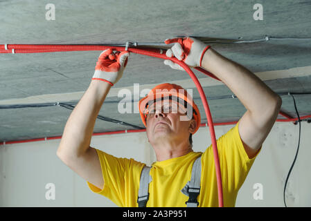 Der Elektriker ist zur Festsetzung einer elektrischen Wellrohr an der Decke. Stockfoto