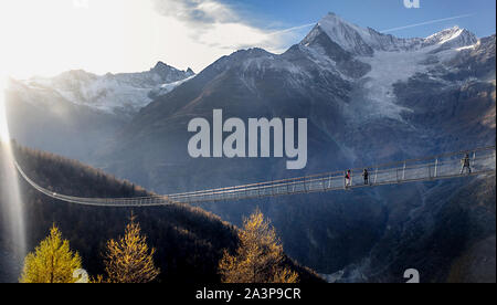 Randa, Schweiz, 8. Oktober 2019: lange Hängebrücke in Zermatt über Landschaft verschneite Berge Wald bei Sonnenuntergang. Suspension Bridge. Lange Brücken. Stockfoto