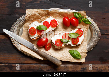 Bruschetta mit Frischkäse, Cherry Tomaten und Basilikum auf einem Holztisch Stockfoto