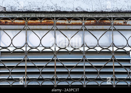 Dekorativer Sicherheit Gitter am Fenster mit sich wiederholenden Herzförmig und ein Detail des Alten zerbröckelt geknackt Verputzte Wand Stockfoto
