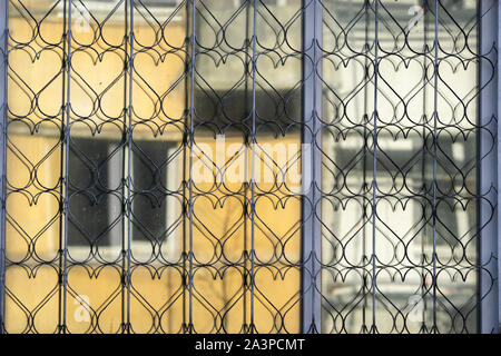 Openwork Metallgitter mit Herz Formen für die Sicherheit auf dem Fenster. Es gibt Raster Reflexionen über das Fenster Glas Stockfoto