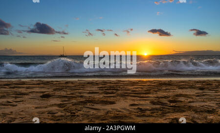Strand Sonnenuntergang mit Wellen und ein Boot auf dem Wasser in Kihei, Maui, Hawaii. Stockfoto
