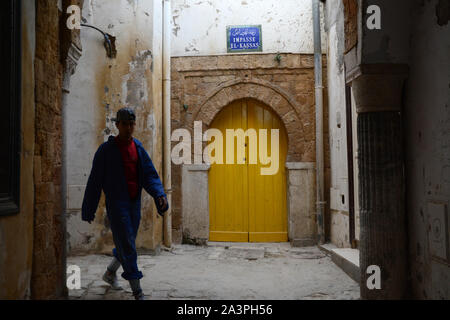 Ein teenager-Tunesischen Arbeiter tragen eine einheitliche und Baseball Cap zu Fuß durch die Gassen der Medina von Tunis, Tunesien. Stockfoto