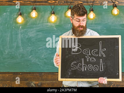 Zurück zum Konzept der Schule. Lehrer in Brillen holding Schiefertafel mit Satz zurück in die Schule, in der es geschrieben. Mann mit Bart und Schnurrbart auf überrascht Gesicht begrüßt Studenten, schwarzes Brett für den Hintergrund. Stockfoto