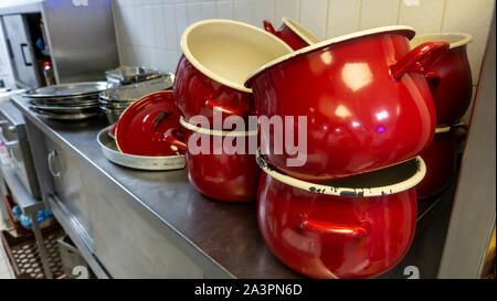 Alte rote abgesplitterte Kochtöpfe im industriellen Küche mit anderen Küchenutensilien Stockfoto