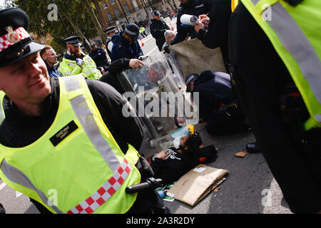 Ein Mitglied des Klimawandels in der Aktivistenbewegung, Aussterben Rebellion (XR) wartet auf Whitehall festgenommen werden, als Polizeibeamte Power Tools verwenden, um ihn von einem anderen Demonstrator am dritten Tag von der Gruppe "Internationale Rebellion" in London zu trennen. Polizisten weiterhin klare Demonstranten und Zelten von Standorten in Westminster, mit Aktivistinnen in zum Verschieben in einen speziellen Protest Bereich um Nelson's Column auf den Trafalgar Square oder Gesicht Verhaftung gewarnt worden. Ähnliche Blockaden vom Aussterben Rebellion im April, an Standorten mit der Oxford Circus und Waterloo Bridge, sah mehr als 1. Stockfoto