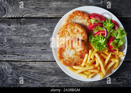 Türkei Burger gebraten serviert mit Salat Tomate Salat und Pommes frites auf einem weißen Teller auf einem rustikalen Holztisch, horizontale Ansicht von oben, flatlay, Stockfoto