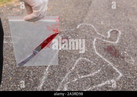 Konzept der Crime Scene Investigation, Detektiv oder Ermittler holding Beweis Tasche mit blutigen Messer in der Tasche und Kreide skizziert toten Körper als Backgr Stockfoto