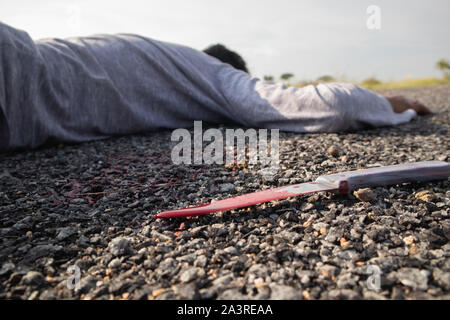 Konzept der Kriminalität Mordszene, selektiver Fokus der Blutigen Messer auf der Straße mit toten Körper als Hintergrund zur Festlegung auf der Straße. Stockfoto