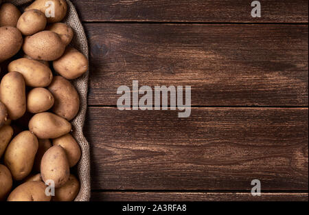 Hintergrund mit rohen Kartoffeln auf Jute Tasche und Holztisch. Platz für Text. Stockfoto