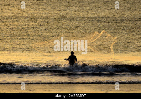 Fischerman warf einen Net am Jimbaran Strand bei Sonnenuntergang. Bali, Indonesien Stockfoto