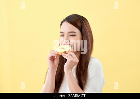 Porträt einer reizende junge asiatische Frau essen Donuts über Gelb Hintergrund isoliert Stockfoto