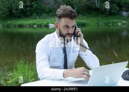 Freiberufliche Arbeit oder Studie Konzept. junger Mann im Büro tragen mit Laptop und am Telefon zu sprechen. Stockfoto