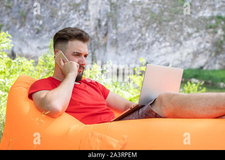 Business Mann auf Smartphone und Laptop Bildschirm. junge Hipster in Konversation auf dem Handy. Bärtige stattlicher Mann mit Handy Stockfoto