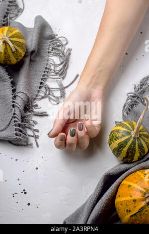 Trend Maniküre im Herbst Farben auf einem grauen Tisch neben Kürbisse und einem grauen Schal Stockfoto