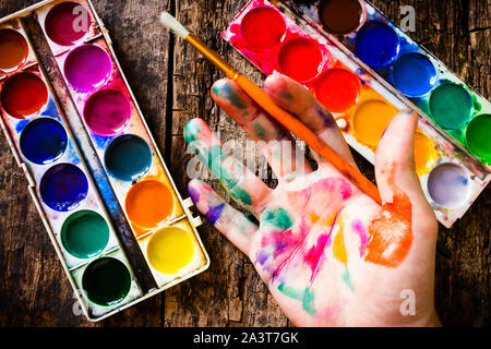 Aquarell Pinsel die Hand des Künstlers in der multi zu malen - farbige Lackierung auf Holz Hintergrund mit einem Besen Stockfoto