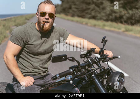 Attraktive brutale Biker mit sigar posiert auf Motorrad Stockfoto