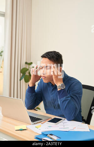 Das Gefühl erschöpft. Frustrierte junge Bart Mann massieren den Kopf und die Augen, während er an seinem Arbeitsplatz im Büro geschlossen Stockfoto