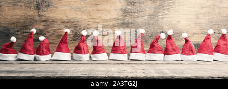 Hüte von Santa in einer Reihe auf einem rustikalen Holztisch, Panoramaaussicht Stockfoto