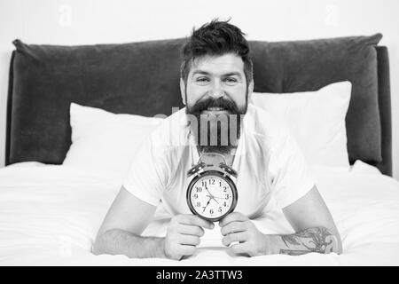 Warum sollten Sie früh aufstehen jeden Morgen. Nutzen für die Gesundheit der Früh aufstehen. Aufwachen frühzeitig, mehr Zeit für die Vorbereitung und zeitgerecht erfolgen. Hipster bärtiger Mann im Bett lagen mit Wecker. Zeit aufzuwachen. Stockfoto