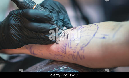 Professionelle Tätowierer macht ein Tattoo auf die Hand eines jungen Mannes, close-up. Tätowierer, Tattoo Tattoo Salon. Prozess der Herstellung tattoo bei der Tat Stockfoto