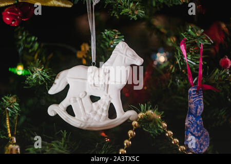 Weihnachten Spielzeug in Form einer weißen Keramik antik Schaukelpferd mit Geschenken auf einem geschmückten Weihnachtsbaum. Close-up. Stockfoto